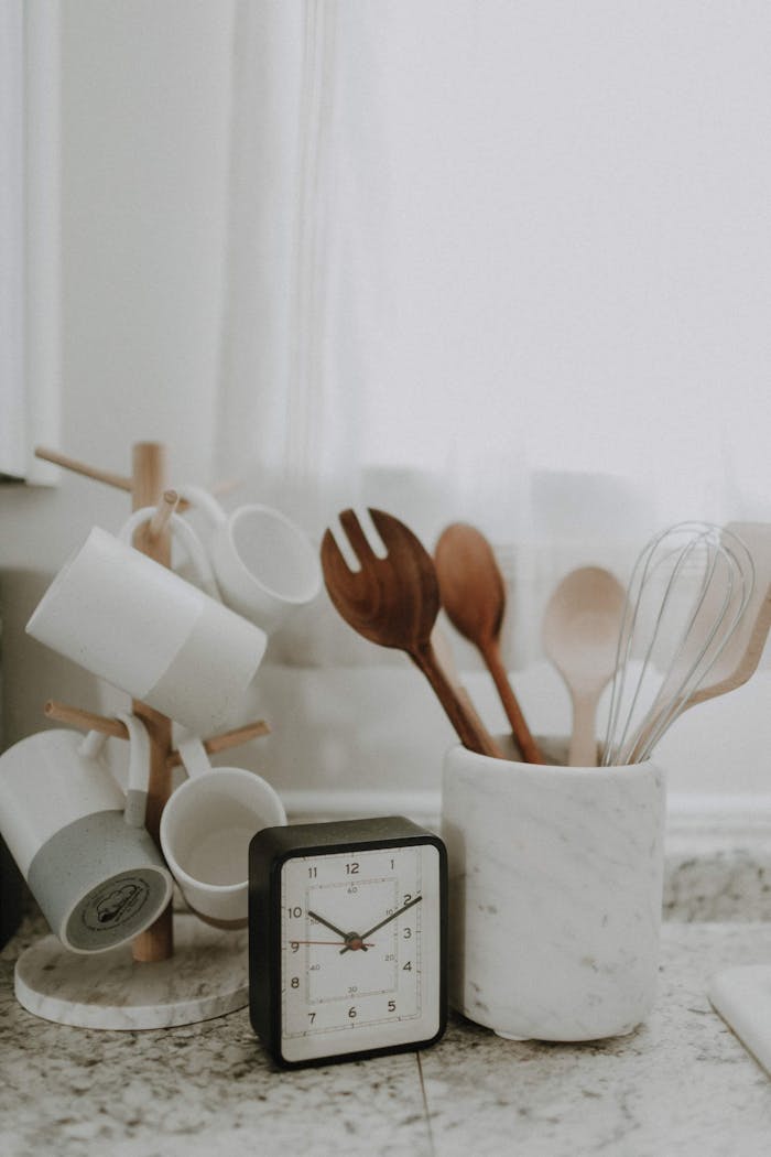 A minimalist kitchen scene featuring utensils, mugs, and a clock on the counter.